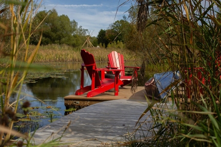Red Adirondack chairs sit on a dock by a lake